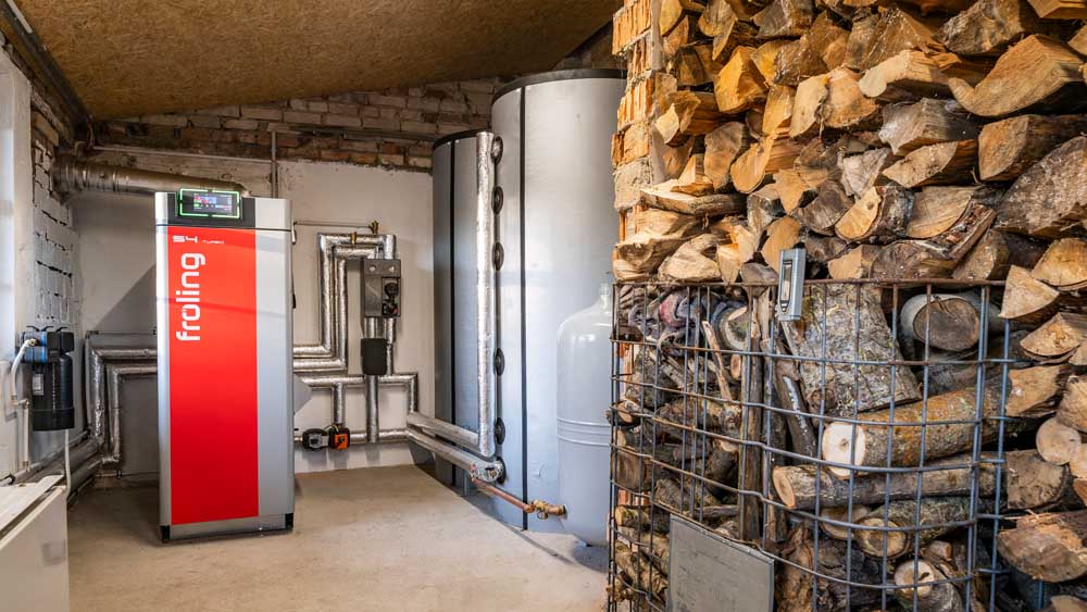 Holzscheitkessel von Fröling mit Pufferspeichern und aufgestapelten Holzscheiten