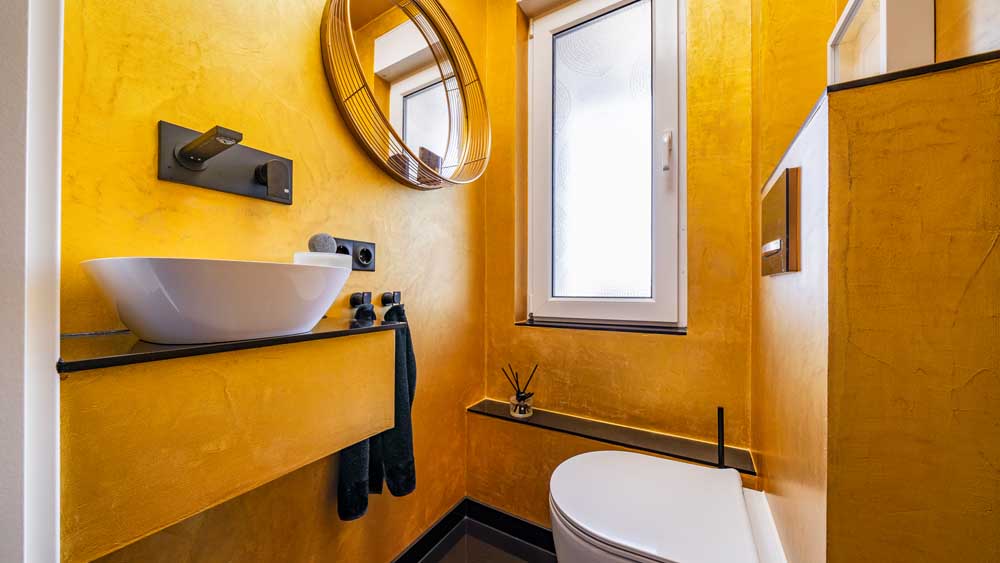 Blick ins Bad mit glodfarbener Wandbeschichtung